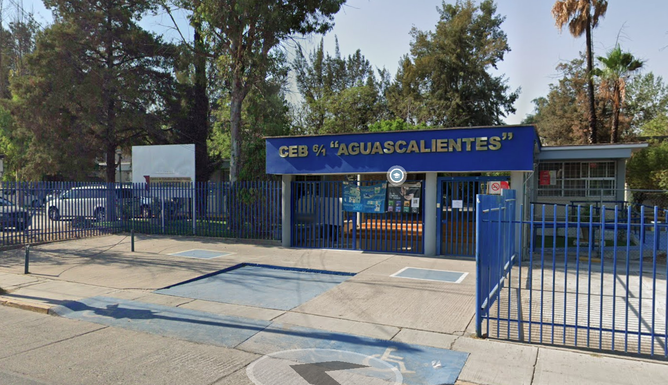 Fotografía donde se muestra la fachada del plantel color azul y sobre ella resalta, en letras doradas, el texto C E B, 6, 1 AGUASCALIENTES. El edificio está rodeado por una reja del mismo color de la fachada y a su alrededor un área verde. 